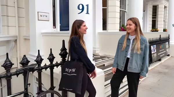Dos estudiantes están frente a un edificio en el campus de MPW London y conversan.