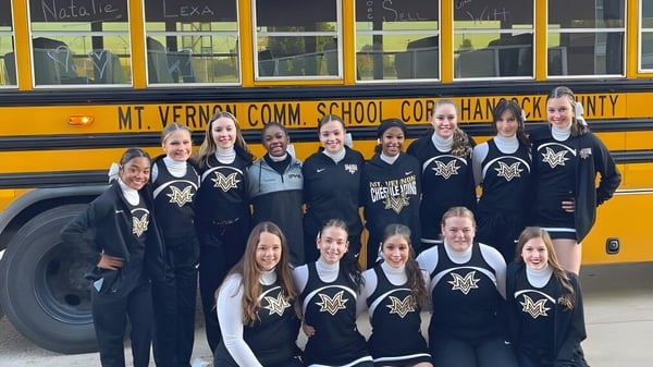Estudiantes de la Mt. Vernon High School posan en uniforme frente a un autobús escolar amarillo con la inscripción Mt. Vernon Comm. School Corp.