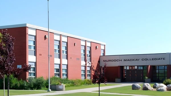 El edificio de ladrillo de varios pisos del Murdoch Mackay Collegiate con césped y piedras en primer plano.