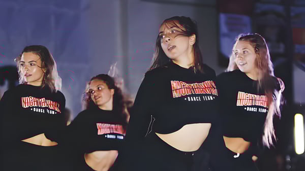 Un grupo de alumnas de la Murietta Valley High School lleva sudaderas negras con capucha con un logo especial en una habitación débilmente iluminada.