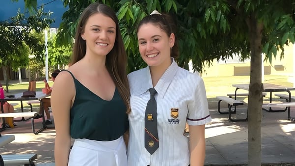Dos estudiantes están al aire libre en el campus del Murrumba State Secondary College frente a árboles y un edificio.
