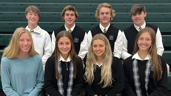 Un grupo de estudiantes de la Muskegon Catholic Central High School posan juntos frente a una pared verde en el edificio escolar.