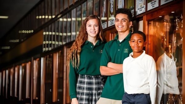 Tres estudiantes de la Muskegon Catholic Central High School están juntos en el pasillo de la escuela frente a los casilleros.
