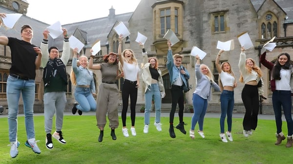 Un grupo de estudiantes del Myddelton College está en un prado frente a un edificio histórico y saluda con banderas blancas.
