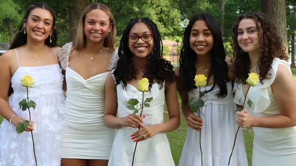 Cinco estudiantes de la Nansemond-Suffolk Academy están con rosas amarillas en un área exterior verde.