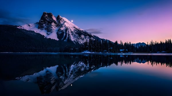 Un tranquilo lago de montaña refleja las cumbres nevadas y el cielo de la tarde en el paisaje cerca de la Napanee District Secondary School.