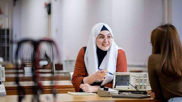 Una mujer con hijab está en un mostrador de recepción hablando con una persona en el campus del National Mathematics and Science College.