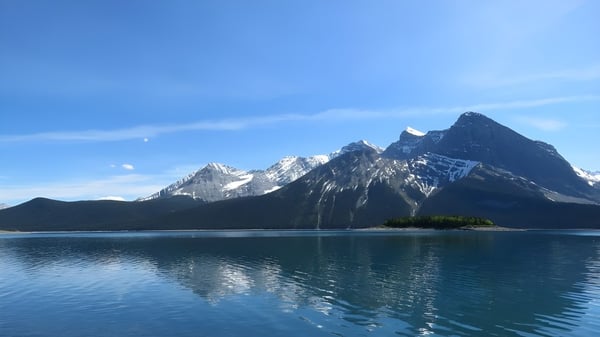 Paisaje montañoso con picos cubiertos de nieve y un lago espejo en primer plano cerca de la National Sport School.