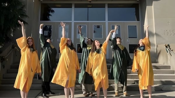 Estudiantes de la Nativity BVM High School están en túnicas coloridas en la escalera y levantan los brazos de manera sincronizada.