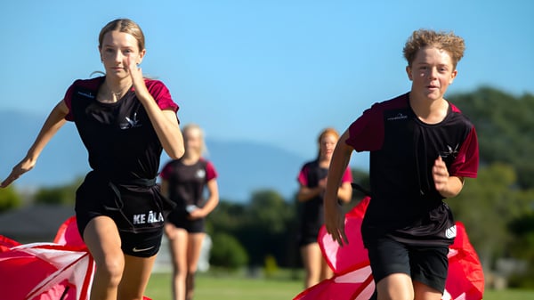 Dos jóvenes atletas corren en un campo de césped frente a un paisaje montañoso en el campus de Nayland College.