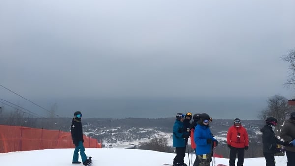 Un grupo de estudiantes de la Nelson High School está de pie en una pendiente nevada frente a un paisaje montañoso neblinoso.