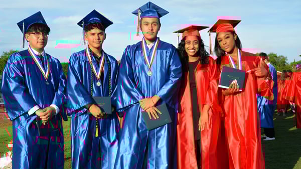 Un grupo de graduados está de pie en el campo verde de la Nepean High School con togas de graduación azules y rojas.