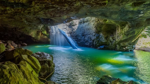 Una cascada de color turquesa fluye sobre rocas cubiertas de musgo hacia un estanque tranquilo en el terreno de la Nerang State High School.