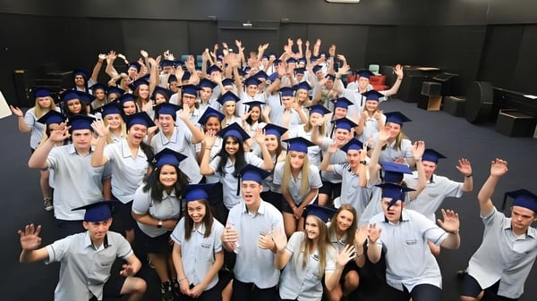 Un grupo de estudiantes de la Nerang State High School levanta las manos en el terreno escolar para celebrar juntos.