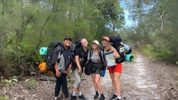 Estudiantes de la Nerang State High School caminan con mochilas por un camino natural.