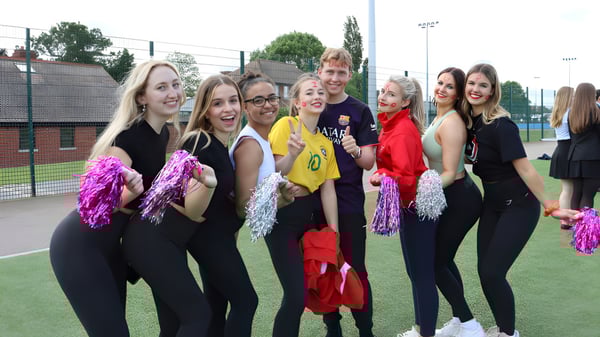 Un grupo de jóvenes estudiantes posando juntas en el campo deportivo de la New Hall School con el edificio escolar y árboles al fondo.