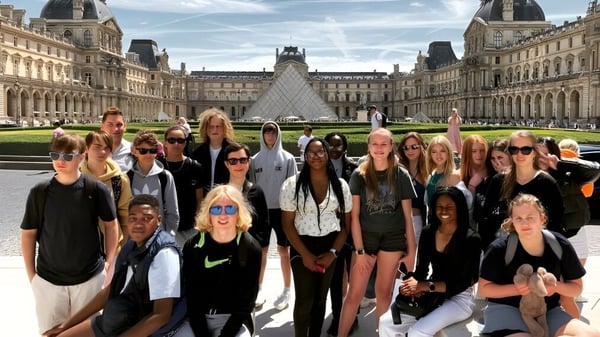 Un grupo de estudiantes de la New Hall School posando frente al Museo del Louvre en París con la pirámide de vidrio al fondo.