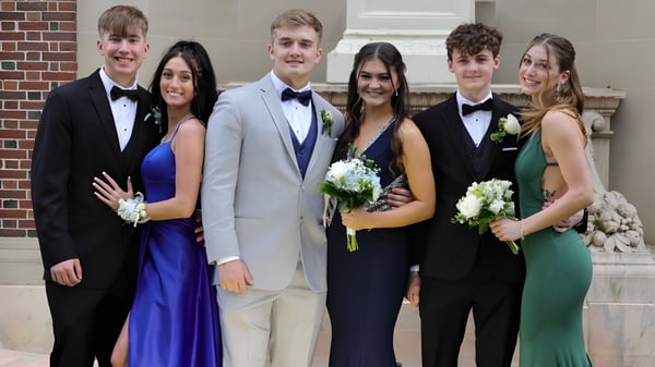 Un grupo de alumnos y alumnas vestidos formalmente está de pie frente a un edificio de ladrillo de la New Hampton School.