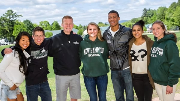 Un grupo de estudiantes de la New Hampton School está afuera en un prado con árboles de fondo.