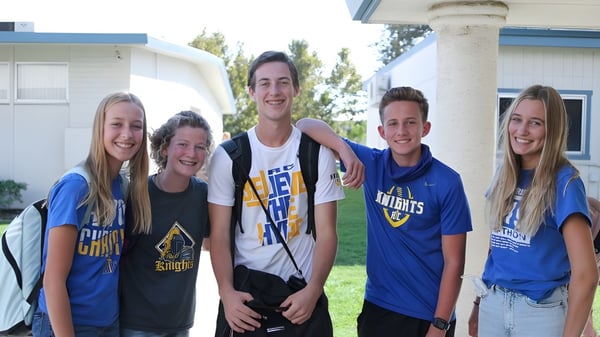 Un grupo de cinco estudiantes está juntos frente a un edificio en el campus de la New Hope Christian School.