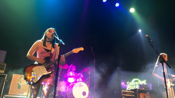 Una estudiante de la New Plymouth Girls’ High School toca la guitarra eléctrica en el escenario con una banda y una batería al fondo.