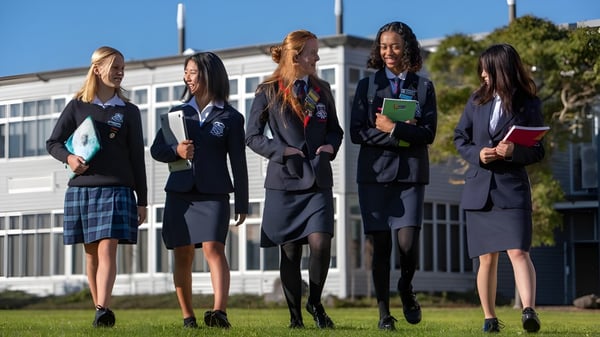 Cinco alumnas de la New Plymouth Girls’ High School están juntas en el campus escolar frente a un edificio.