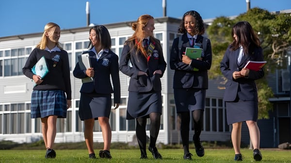Cinco estudiantes en uniformes están juntas en el campus de la New Plymouth Girls’ High School con un edificio al fondo.
