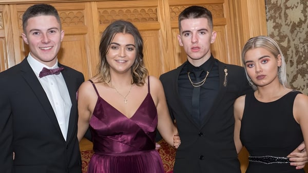 Cuatro personas bien vestidas posan juntas en una sala de madera ricamente decorada en el campus del Newbridge College.