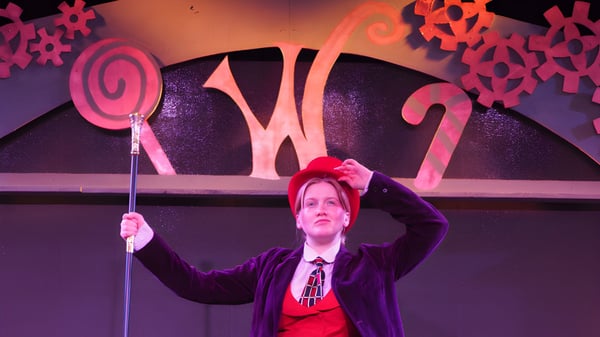 Una persona vestida de púrpura está frente al colorido y abstracto telón de fondo del escenario en el campus de la Newcastle High School.