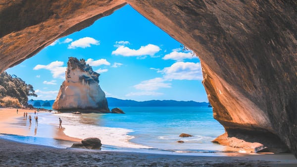 Un arco de roca natural muestra el paisaje costero con playa y montañas cerca del Newlands College.