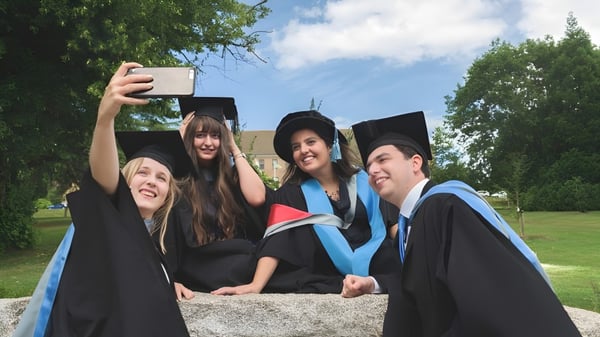 Cuatro graduados del Newstead College en toga académica toman un selfie al aire libre.