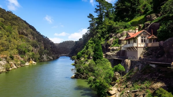 Un pintoresco paisaje fluvial con una casa de madera y montañas en el terreno del Newstead College.