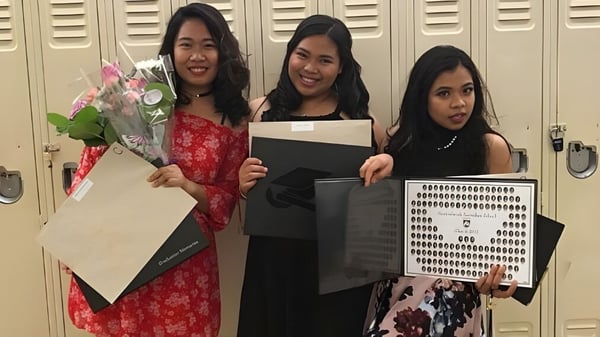 Tres estudiantes de la Newtonbrook Secondary School están frente a los casilleros sosteniendo flores y un cartel.