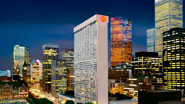 Un rascacielos y otros edificios iluminados se pueden ver de noche frente al edificio de la Newtonbrook Secondary School.