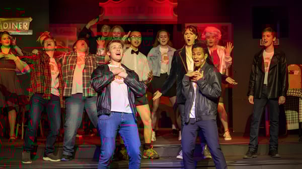 Un grupo de estudiantes de la Newtown School está en un escenario con un fondo rojo durante un evento.