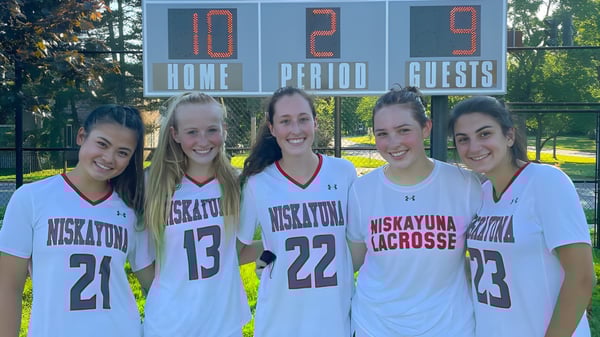 Un grupo de cinco estudiantes de la Niskayuna High School está frente a un marcador durante un juego de lacrosse en el campo deportivo.