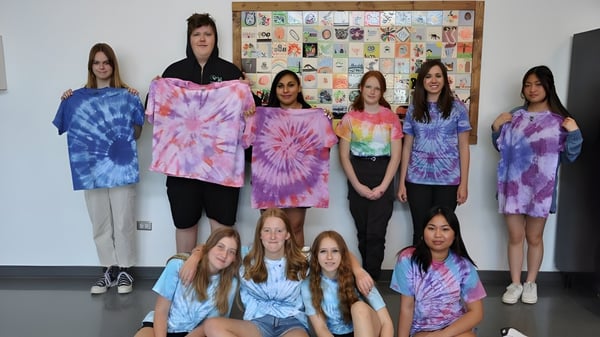 Un grupo de alumnas de la Noble Central School está frente a un tablero de anuncios con diversas obras de arte y decoraciones.