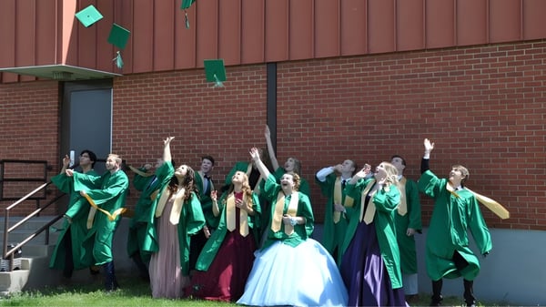 Un grupo de alumnas y alumnos de la Noble Central School está frente a un edificio de ladrillo celebrando juntos con trajes coloridos.