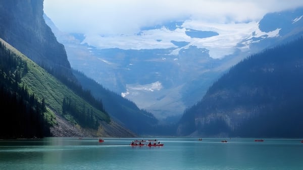 Un tranquilo lago alpino con pequeños botes rojos frente a montañas cubiertas de nieve en los alrededores de la Noble Central School.