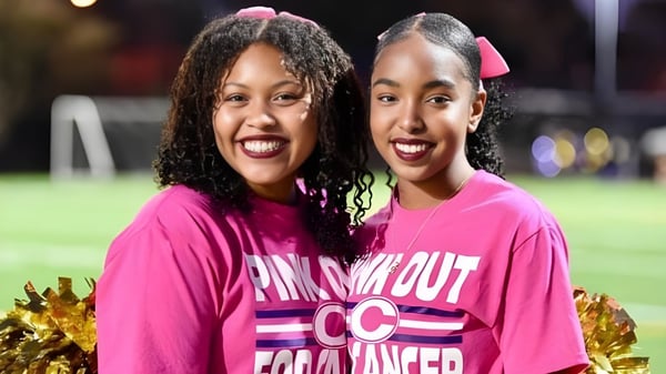 Dos estudiantes de Norfolk Christian Schools posan juntas con pompones en el campo de deportes.