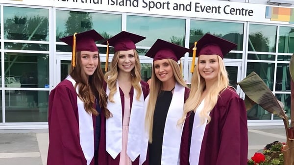 Cuatro estudiantes de la NorKam Secondary School están en togas de graduación frente al Whidbey Island Sport and Event Centre.