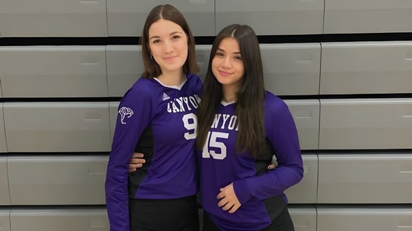 Dos alumnas de la North Canyon High School están frente a un fondo gris en camisetas moradas con los números 15 y 9.