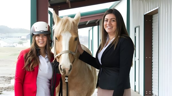 Dos alumnas de la North Central Texas Academy están junto a un caballo en el área exterior frente a un edificio.
