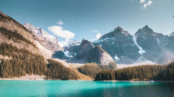 Un lago alpino con montañas cubiertas de nieve y un bosque verde en primer plano cerca de la North Delta Secondary School.