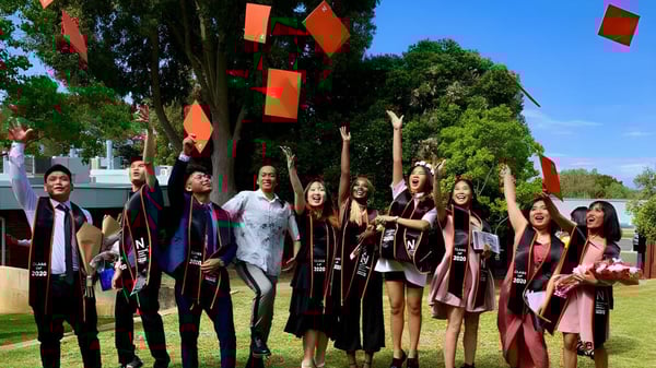 Un grupo de alumnas y alumnos con vestimenta de graduación están al aire libre en el campus de North Lake Senior Campus.