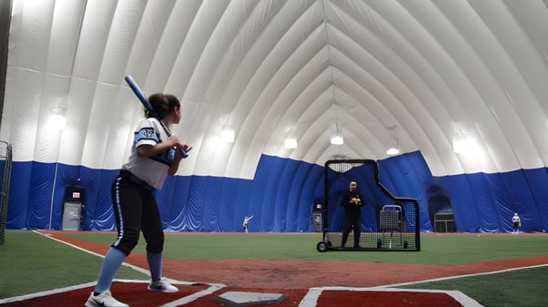Una estudiante de la Northeastern Wisconsin Lutheran High School está en el campo de béisbol frente a una estructura inflable azul y blanca.