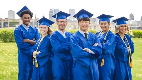 Los graduados de la Northeastern Wisconsin Lutheran High School en togas azules están de pie frente a un paisaje urbano.