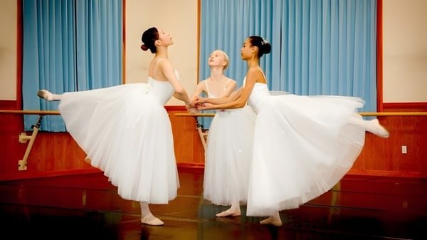 Tres bailarinas en tutús blancos están sobre el suelo de madera de la Northern Academy frente a cortinas azules.