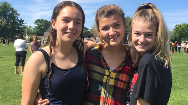 Tres alumnas están de pie sobre un área cubierta de césped frente a unos árboles en el campus de la Northern Collegiate Institute & Vocational School.