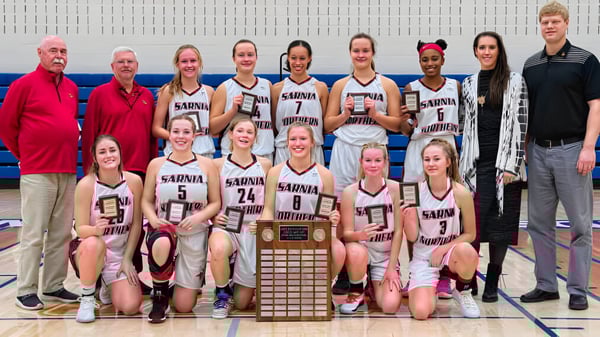 Un grupo de jóvenes jugadoras de baloncesto de la Northern Collegiate Institute & Vocational School sostiene un trofeo en el gimnasio.